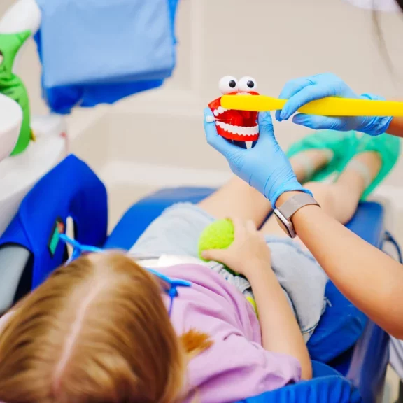 Chirurfien-dentiste rassurant et expliquant le brossage de dent à une enfant